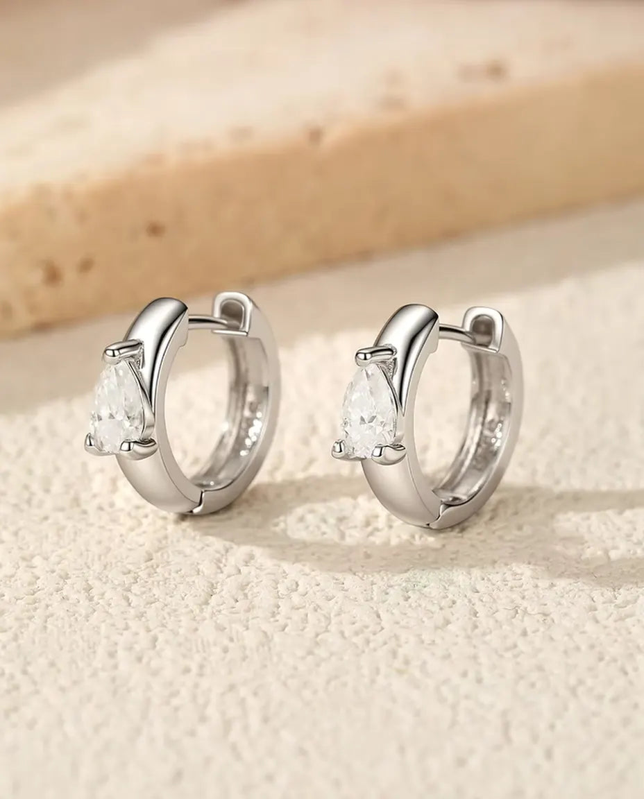 Moissanit Huggie Creolen mit Tropfenstein aus 925 Sterlingsilber - das Paar nebeneinander stehend auf heller Strukturfläche