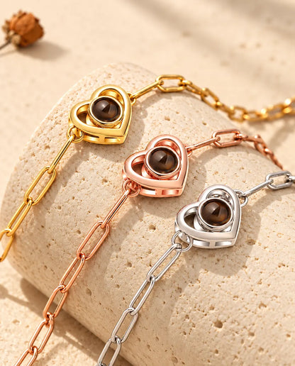 Doppelherz-Armbänder in Gold, Roségold und Silber über einem Travertinblock