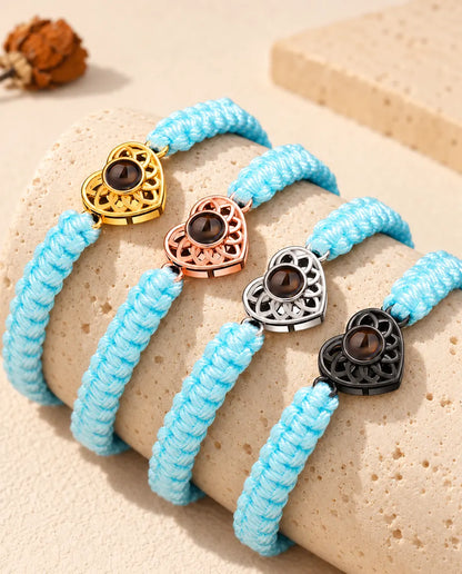 Armbänder mit hellblauem Flechtband nebeneinander auf Travertin, das Herz in jeder Charm-Farbe