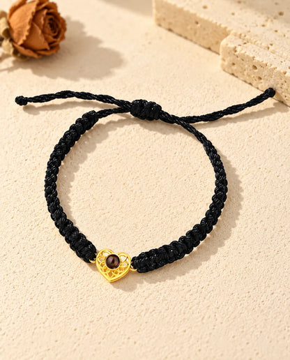 Draufsicht: Armband mit goldfarbenem Herz an schwarzem Flechtband, mit Schiebeknoten und Bandenden