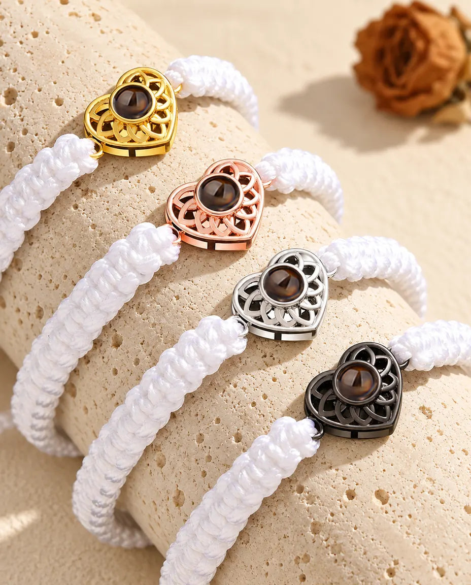 Vier Armbänder mit weißem Flechtband und Herz in Gold, Roségold, Silber und Schwarz auf Travertin