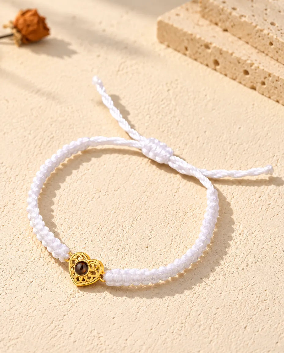 Armband mit weißem Flechtband, goldfarbenem Herz und Schiebeknoten auf hellem Gips