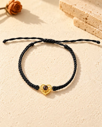 Draufsicht: Armband mit goldfarbenem Herz an schmalem schwarzem Flechtband, mit Schiebeknoten und Bandenden