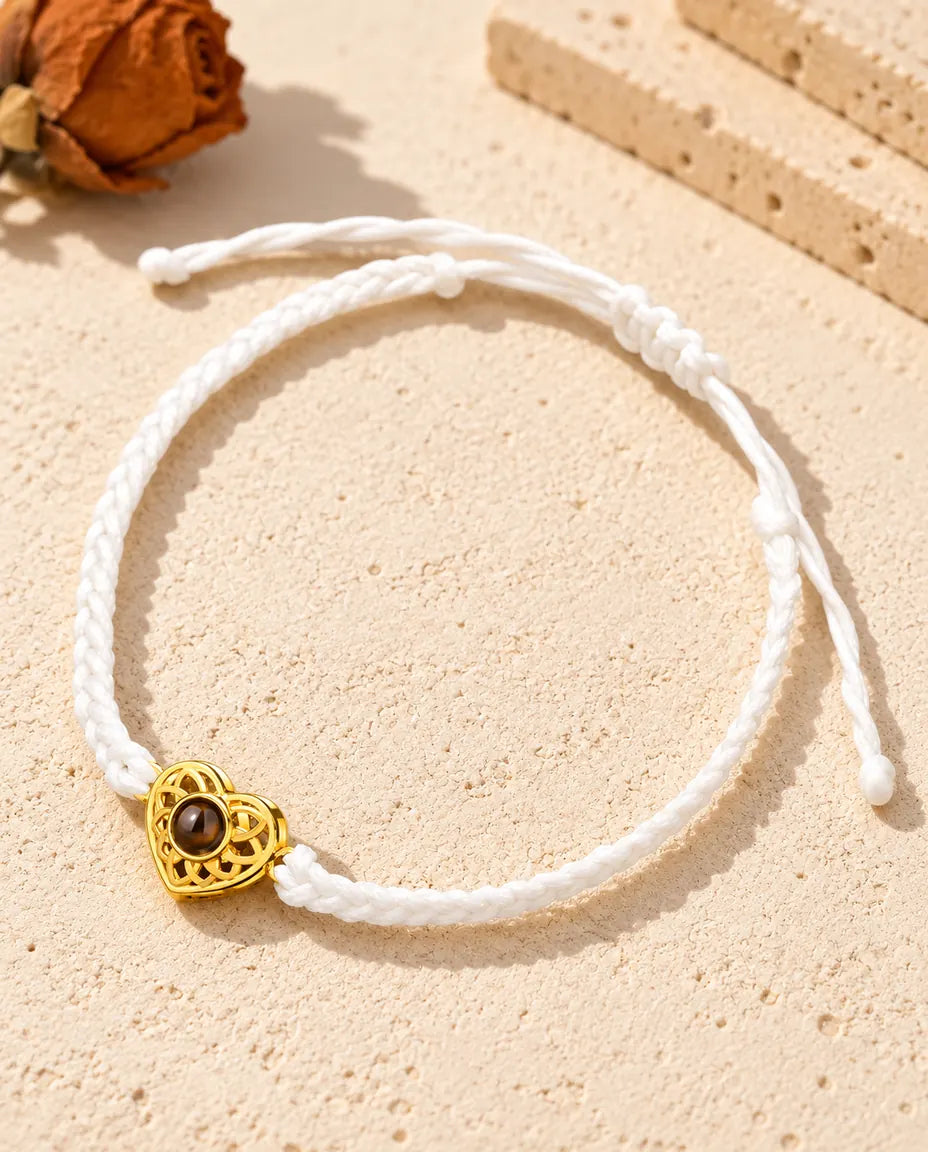 Armband mit schmalem weißem Flechtband, goldfarbenem Herz und Schiebeknoten auf hellem Gips