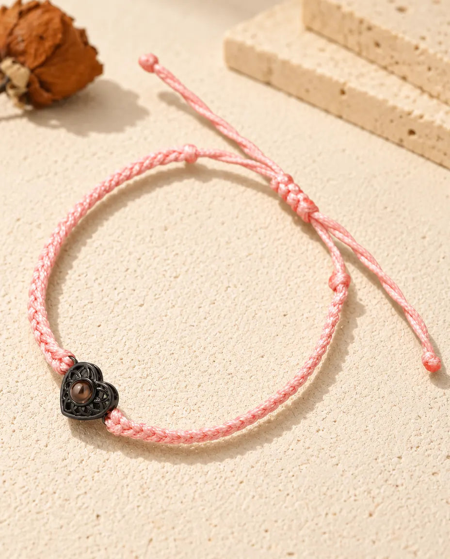 Armband mit schmalem rosa Flechtband, schwarzem Herz und braunem Bildstein auf hellem Gips