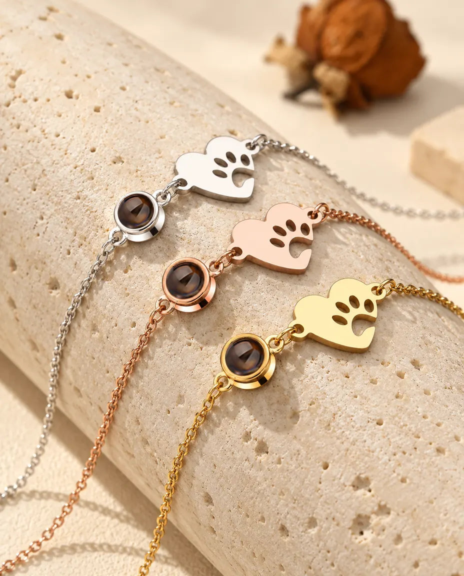 Drei Pfoten-Herz-Armbänder in Silber-, Roségold- und Goldfarben über einem Travertinblock