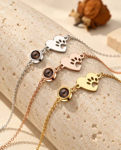 Drei Pfoten-Herz-Armbänder in Silber-, Roségold- und Goldfarben über einem Travertinblock