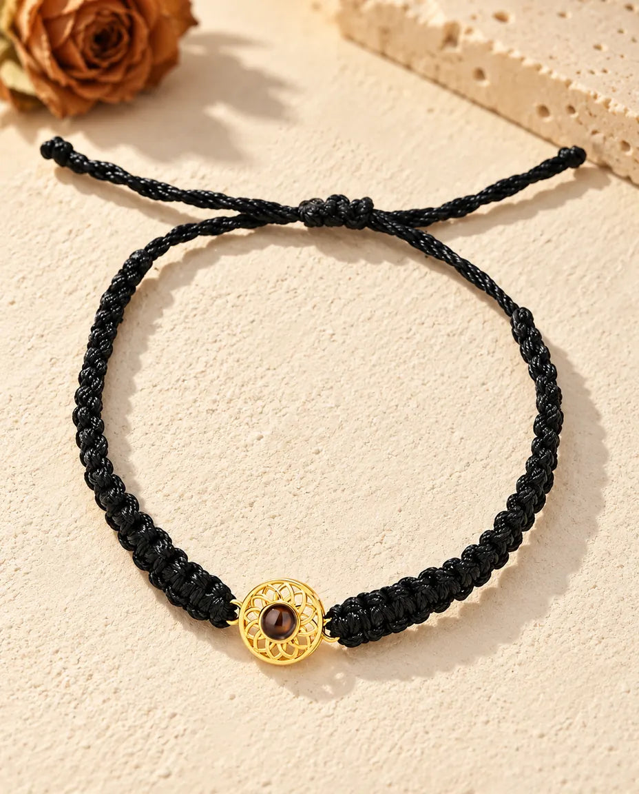 Draufsicht: Armband mit goldfarbenem Rund-Charm an schwarzem Flechtband, mit Schiebeknoten und Bandenden