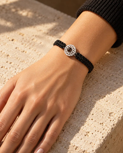 Frau trägt das Armband mit schwarzem Flechtband und silberfarbenem Rund-Charm am Handgelenk im Sonnenlicht