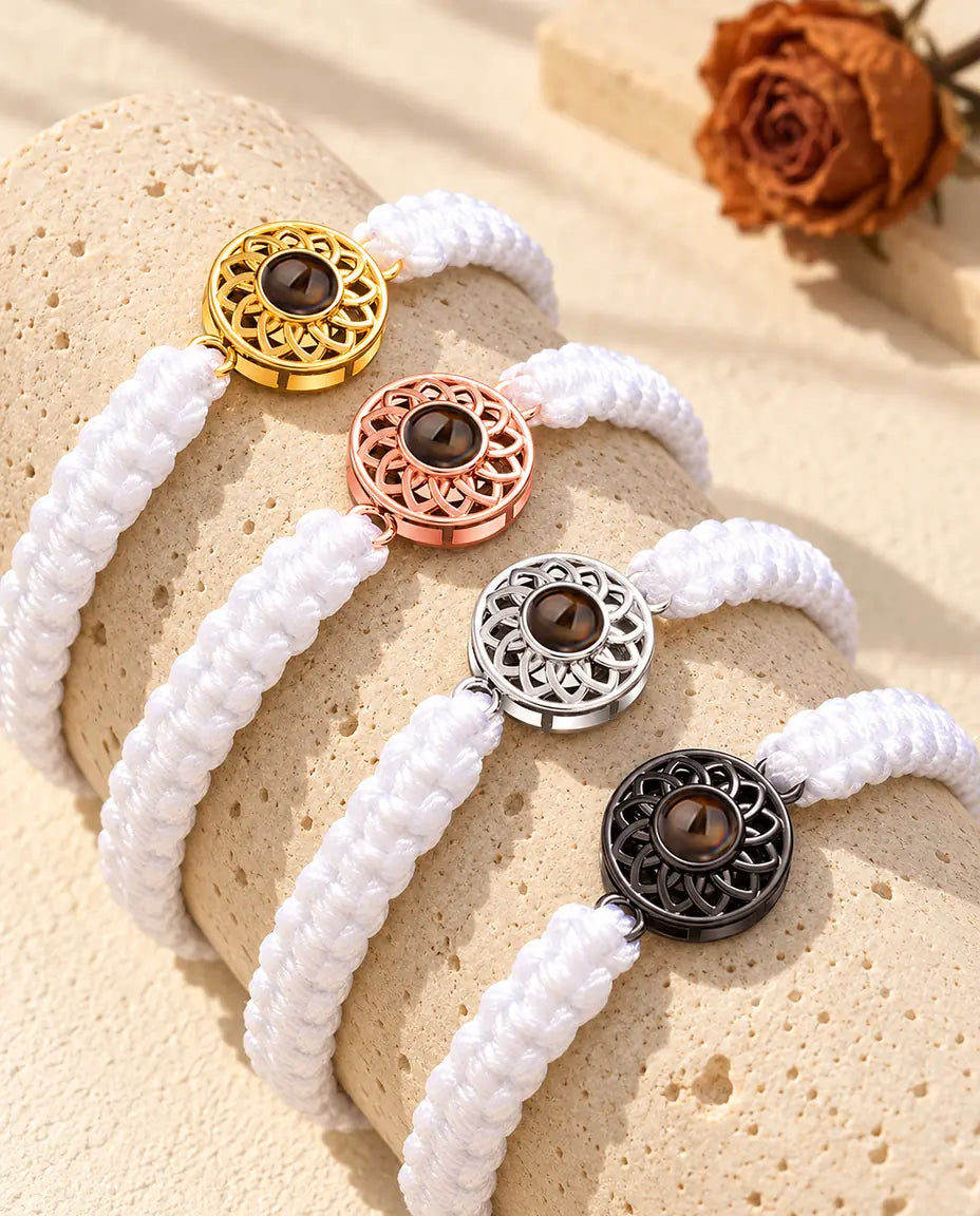 Vier Armbänder mit weißem Flechtband und Rund-Charm in Gold, Roségold, Silber und Schwarz auf Travertin