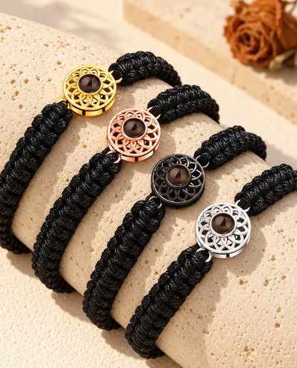 Vier Armbänder mit schwarzem Flechtband und Rund-Charm in allen Charm-Farben über einem Travertinblock