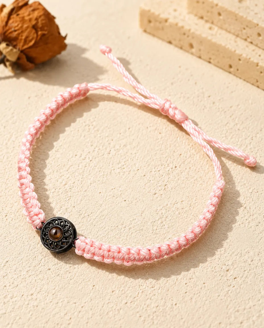 Armband mit rosa Flechtband, schwarzem Rund-Charm und braunem Bildstein auf hellem Gips