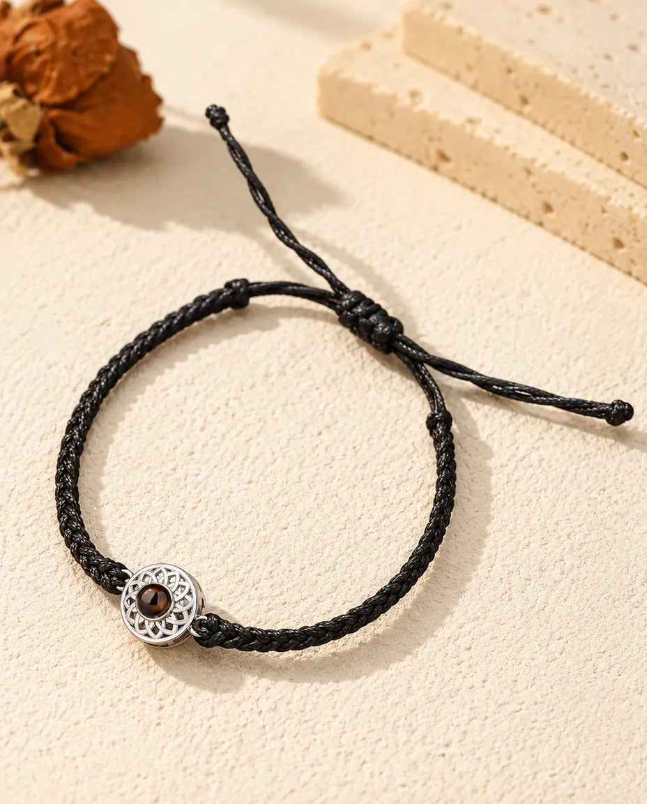 Armband mit Bild im Stein: silberfarbener durchbrochener Rund-Charm an schmalem schwarzem Flechtband auf hellem Gips