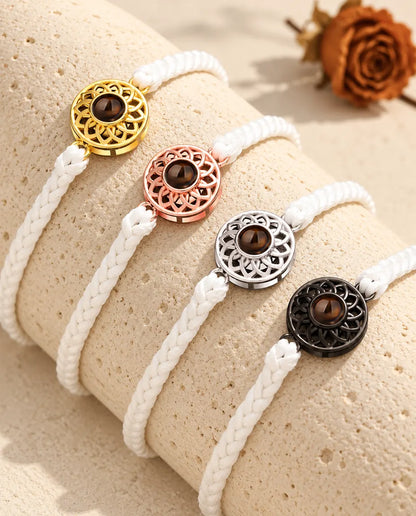 Vier Armbänder mit schmalem weißem Flechtband und Rund-Charm in Gold, Roségold, Silber und Schwarz auf Travertin