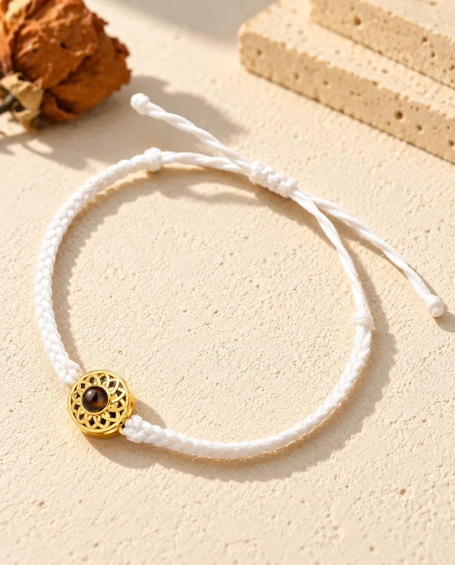 Armband mit schmalem weißem Flechtband, goldfarbenem Rund-Charm und Schiebeknoten auf hellem Gips