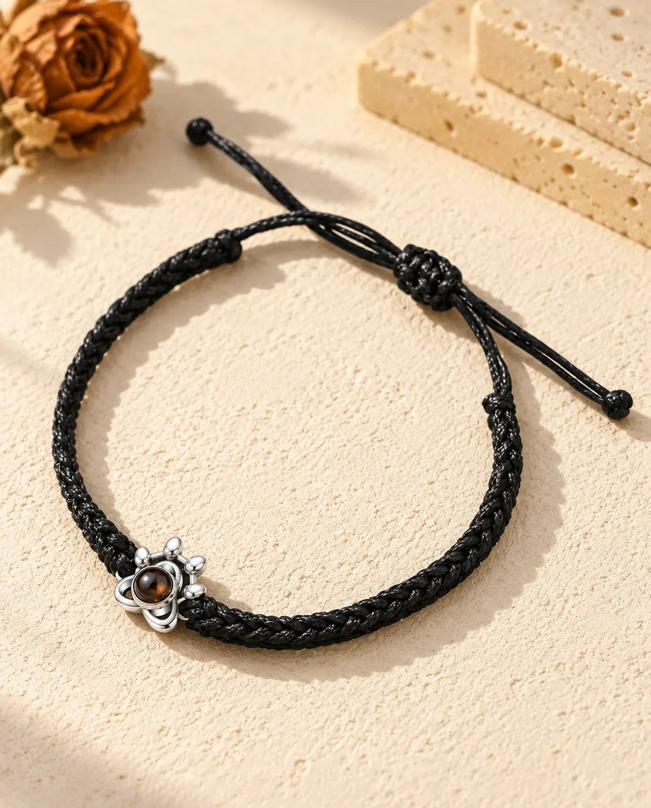 Armband mit Bild im Stein: Pfoten-Charm aus 925er Sterlingsilber an schwarzem Flechtband auf hellem Gips