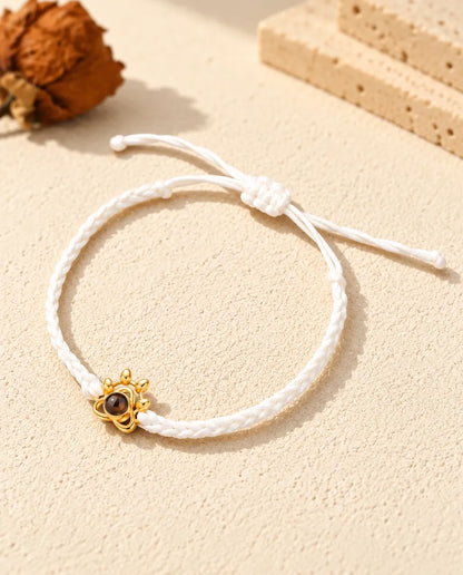 Armband mit weißem Flechtband, goldfarbenem Pfoten-Charm und Schiebeknoten auf hellem Gips