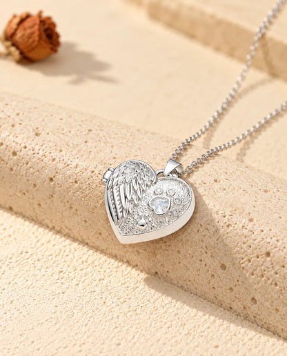 Silberfarbenes Herz-Foto-Medaillon mit Engelsflügel und Pfote als personalisierte Kette, an einen Travertinblock gelehnt
