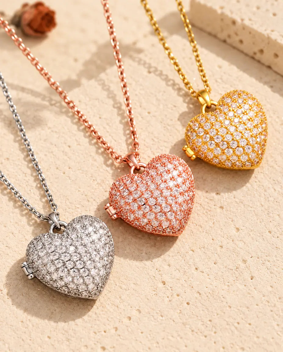 Pavé Herz-Foto-Medaillon in Silber-, Roségold- und Goldfarbe schräg auf cremefarbenem Putz