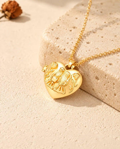 Goldfarbenes Herz-Foto-Medaillon mit zwei Schwestern als Kette an einem Travertinblock