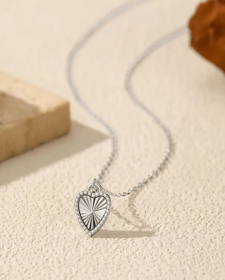 Herz Kette aus 925 Sterlingsilber - Anhänger auf heller Fläche neben einer Travertinplatte