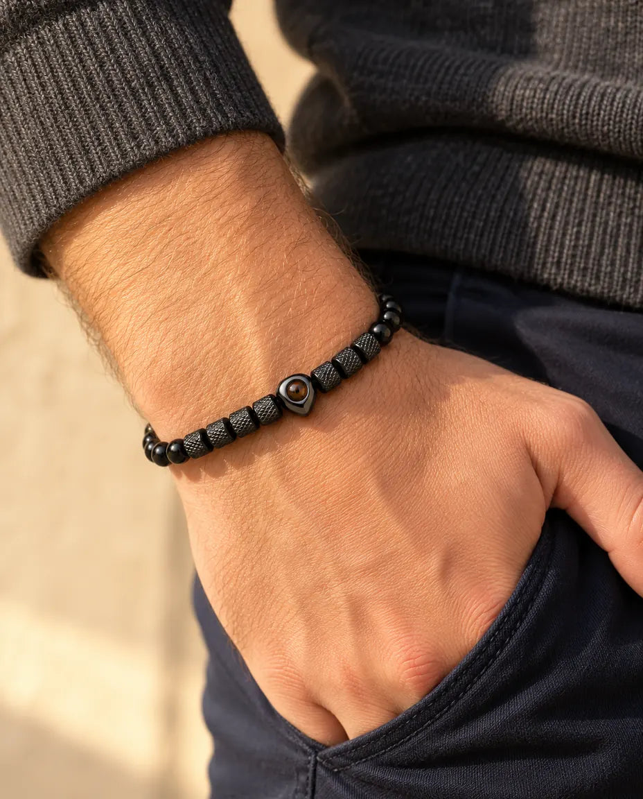 Mann trägt das schwarze Perlenarmband mit Herzperle, den Daumen in der Hosentasche