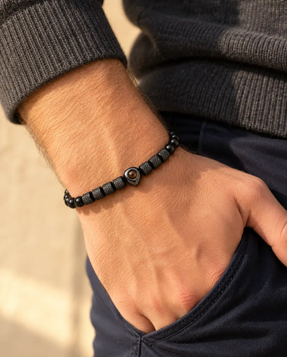 Mann trägt das schwarze Perlenarmband mit Herzperle, den Daumen in der Hosentasche