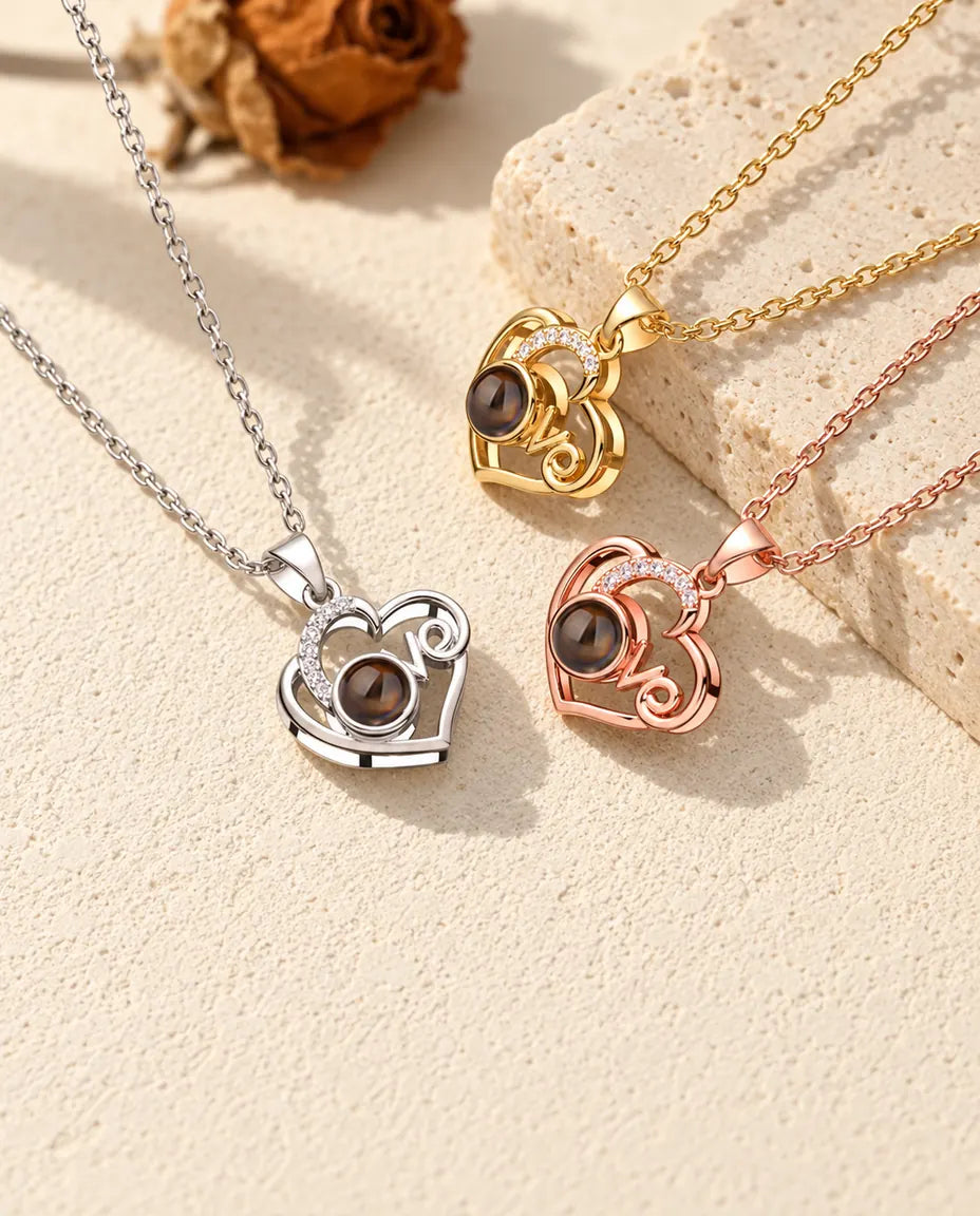 Love-Herz Ketten mit Bild im Stein in Silber-, Gold- und Roségoldfarbe neben einer Travertinplatte