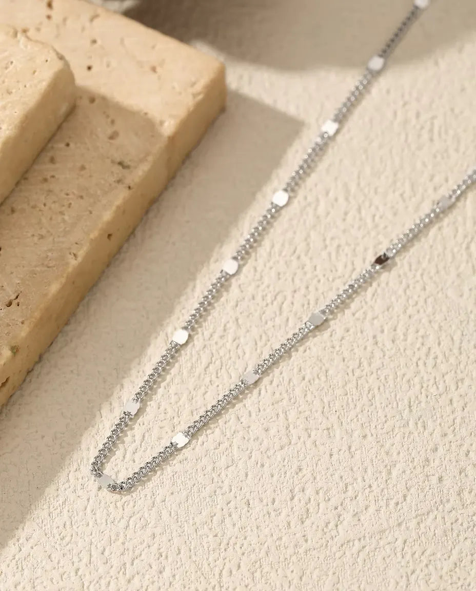 Zarte Kette aus 925 Sterlingsilber mit ovalen Plättchen - über helle Fläche neben einer Travertinplatte gelegt