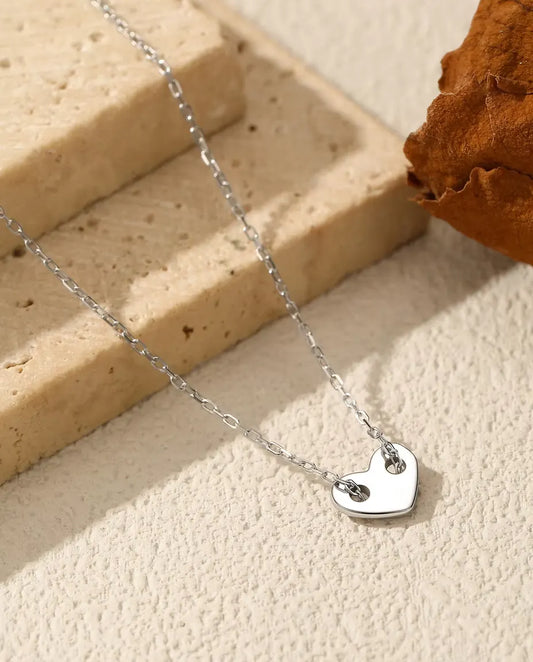 Herz Kette aus 925 Sterlingsilber - Anhänger auf heller Fläche neben einer Travertinplatte