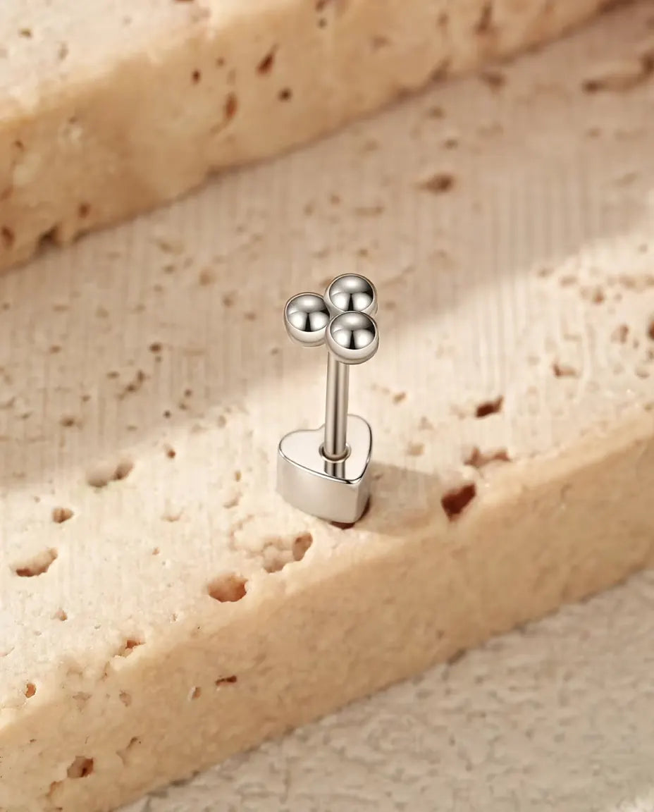 Kleeblatt Ohrstecker mit Silberkugeln aus 925 Sterlingsilber - aufrecht auf dem herzförmigen Verschluss stehend, auf heller Strukturfläche