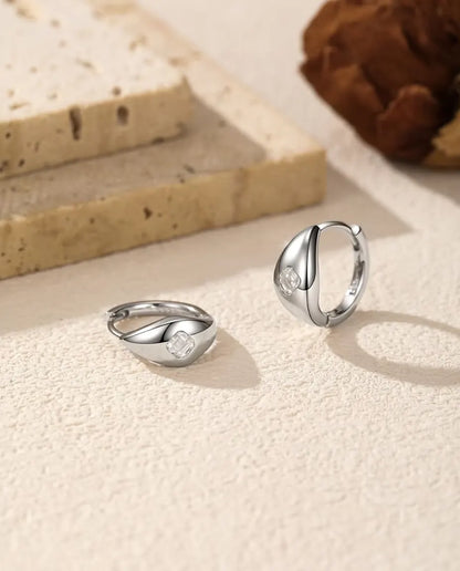 Moissanit Creolen im Asscher-Schliff aus 925 Sterlingsilber - Paar auf heller Strukturfläche, einer liegend und einer stehend
