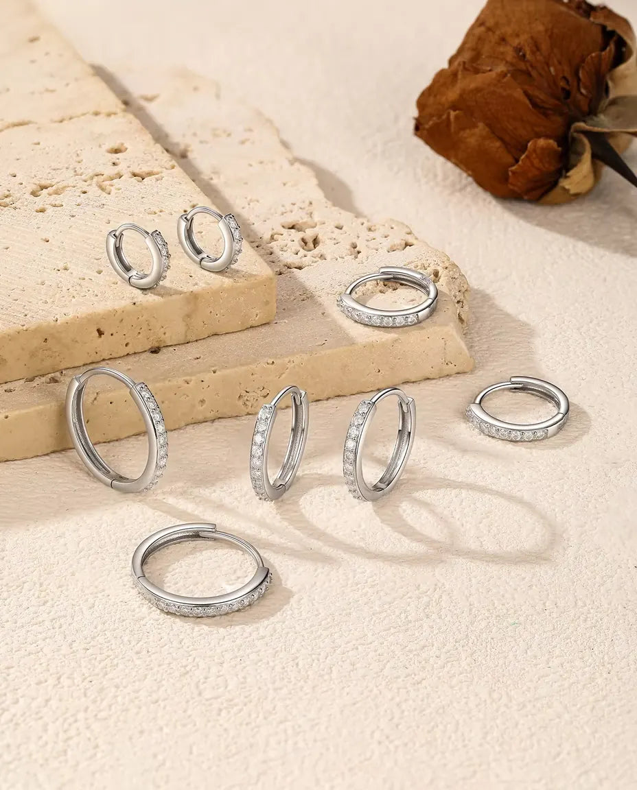 Moissanit Creolen aus 925 Sterlingsilber - fünf Größen auf Travertinplatte und heller Fläche verteilt