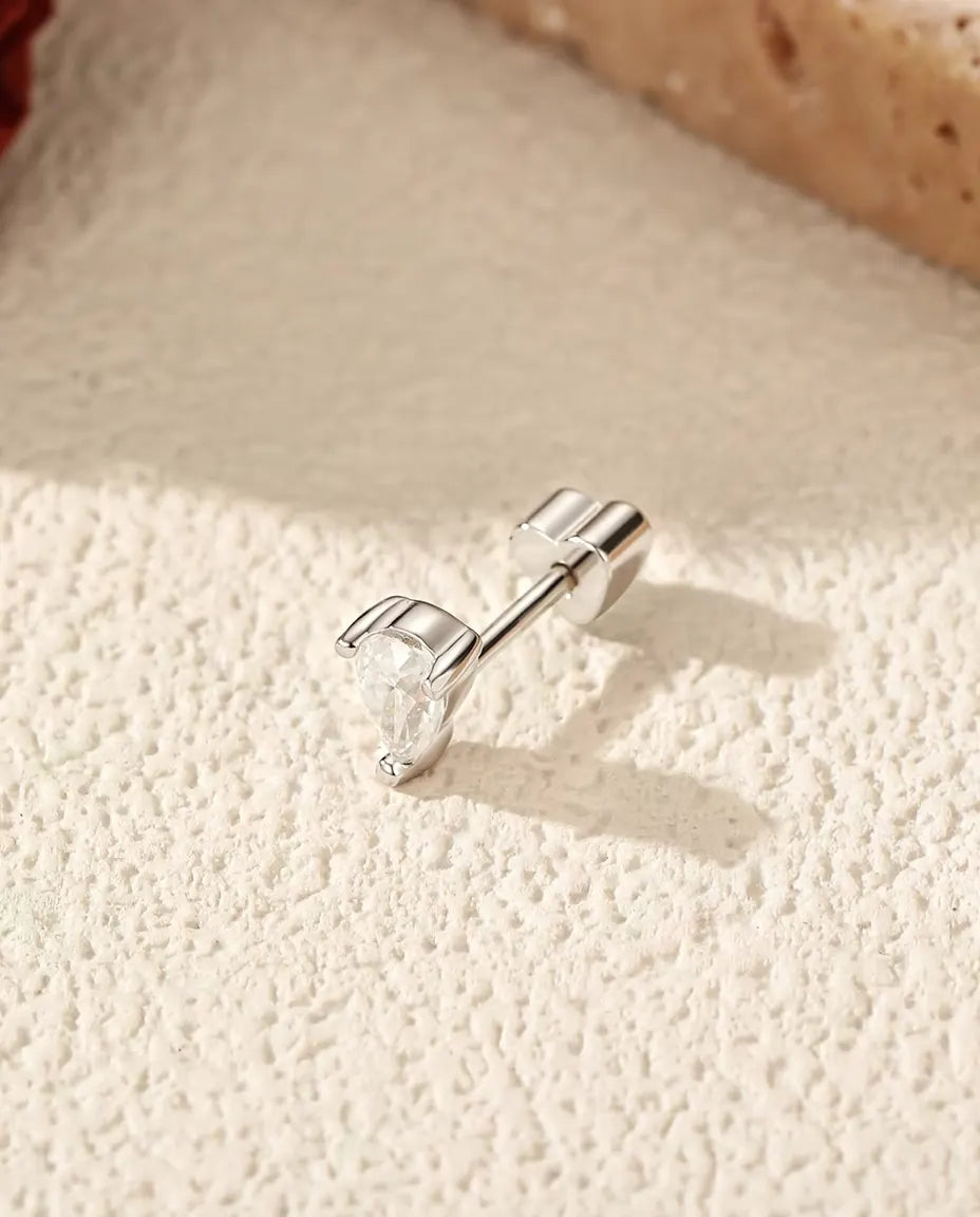 Moissanit Ohrstecker im Tropfenschliff aus 925 Sterlingsilber - seitlich liegend auf heller Strukturfläche, herzförmiger Verschluss auf dem Stift