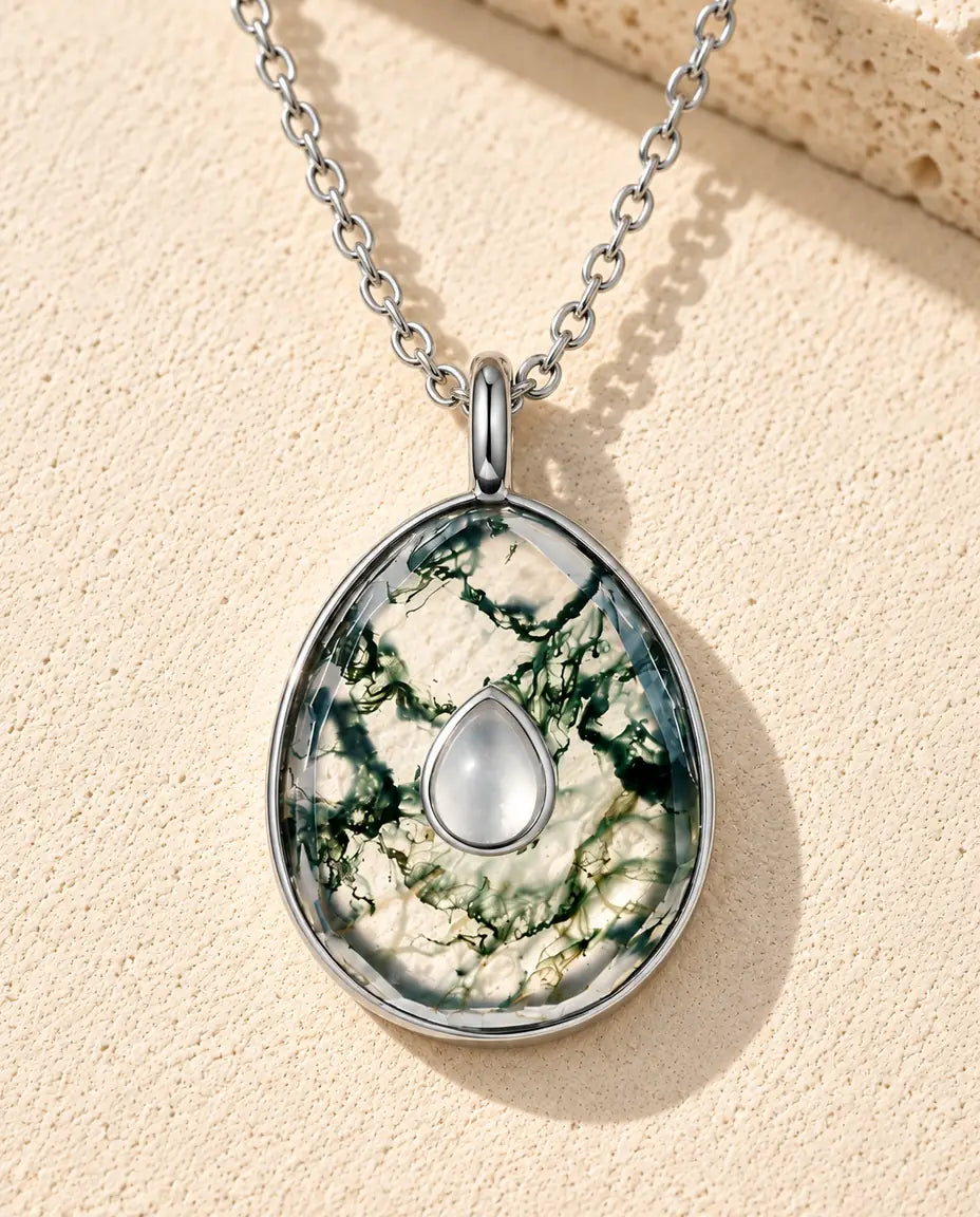 Moosachat Kette mit Ei-Anhänger aus 925 Sterlingsilber - auf heller Strukturfläche neben einem Travertinblock liegend