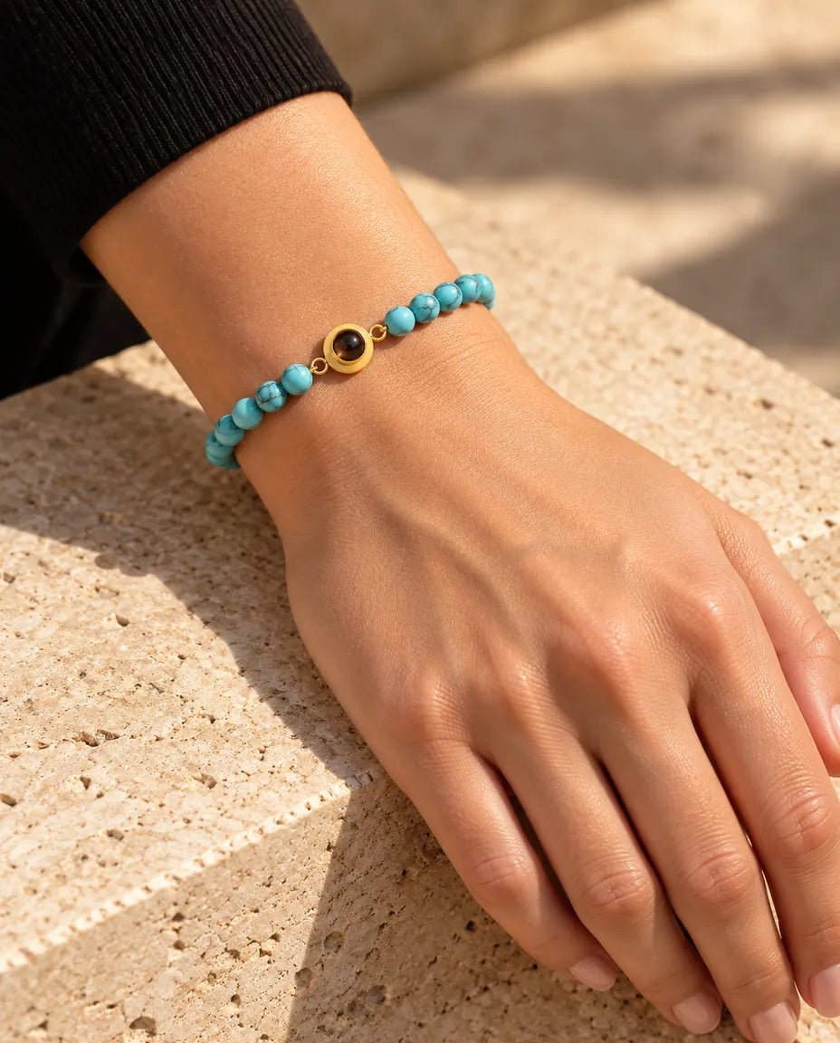 Frau trägt das blau marmorierte Perlenarmband mit goldfarbenem Charm am Handgelenk