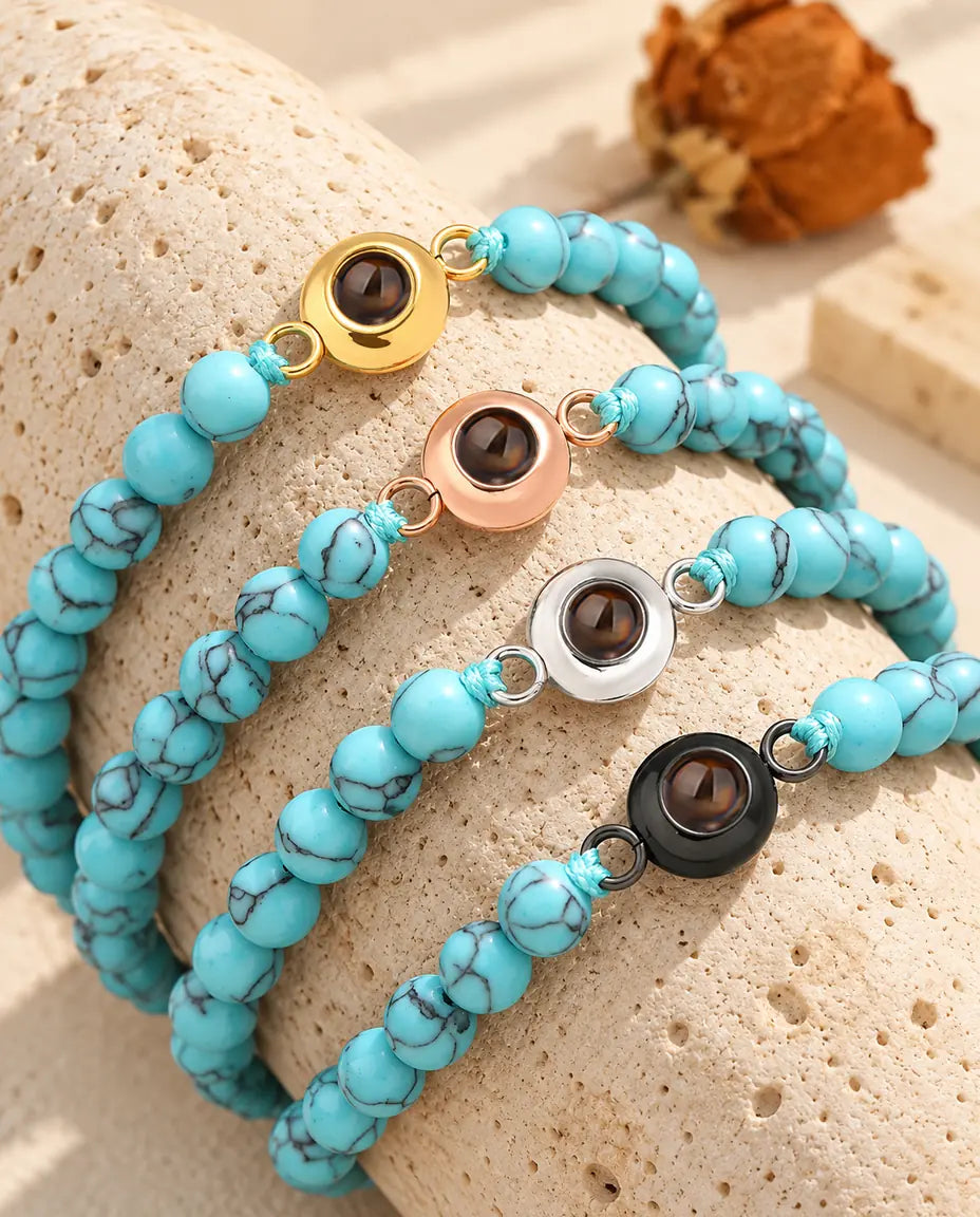 Vier blau marmorierte Perlenarmbänder mit Charm in Gold, Roségold, Silber und Schwarz auf Travertin