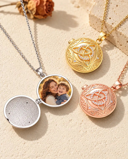 Aufgeklapptes silberfarbenes Medaillon mit keltischem Knoten und Familienfoto neben goldfarbenem und roségoldfarbenem