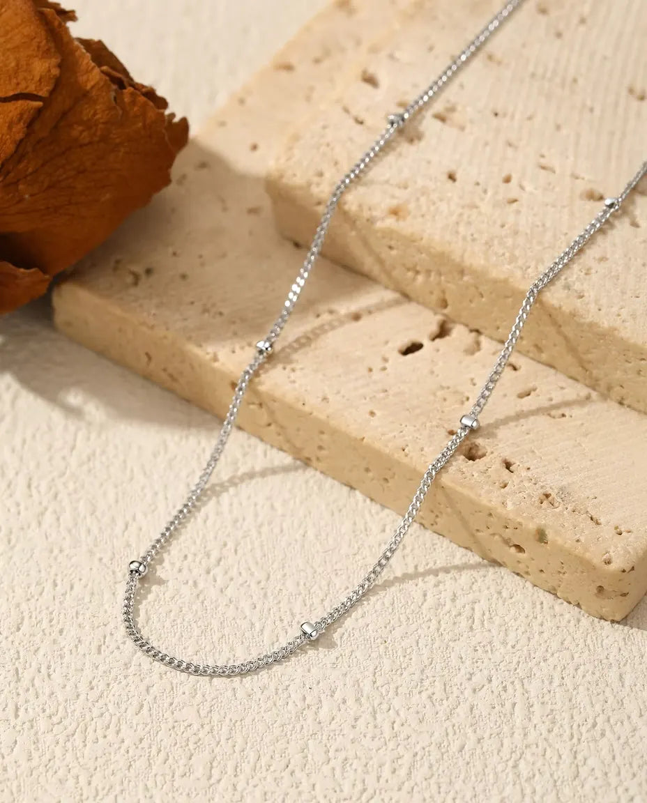 Satelliten Kette aus 925 Sterlingsilber - über helle Fläche neben einer Travertinplatte gelegt