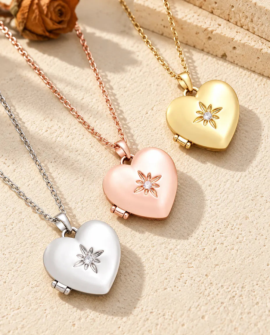 Satiniertes Herz-Foto-Medaillon in Silber-, Roségold- und Goldfarbe schräg auf cremefarbenem Putz