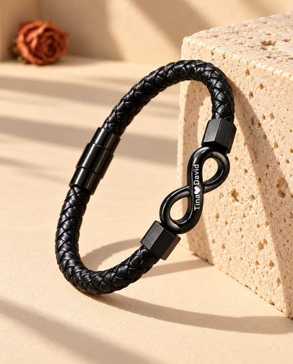 Schwarzes Armband aus geflochtenem Kunstleder mit graviertem Unendlichkeitszeichen, aufrecht an einen Travertinblock gelehnt